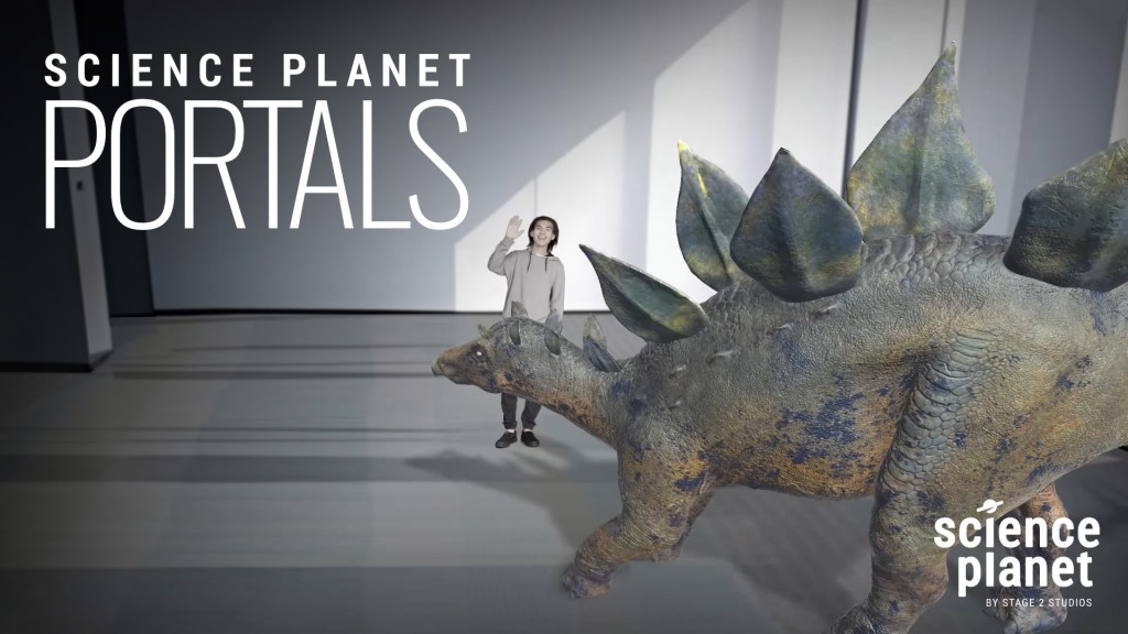Screenshot from the digital exhibit titled Science Planet Portals. A life size 3D stegosaurus dinosaur walks next to a young man through an augmented reality experience projected on a large screen.
